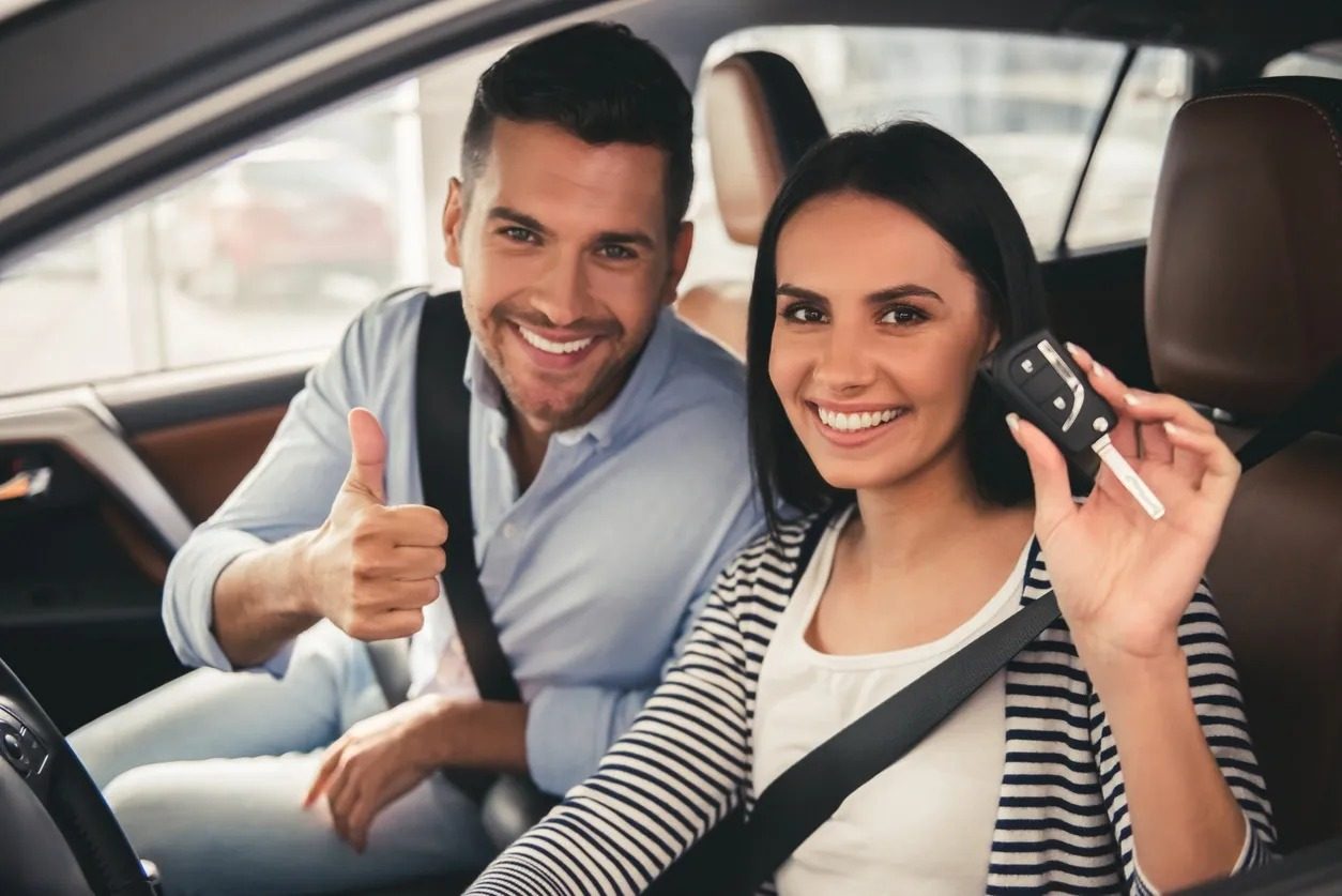 A smiling couple sitting in their car, holding up the car key